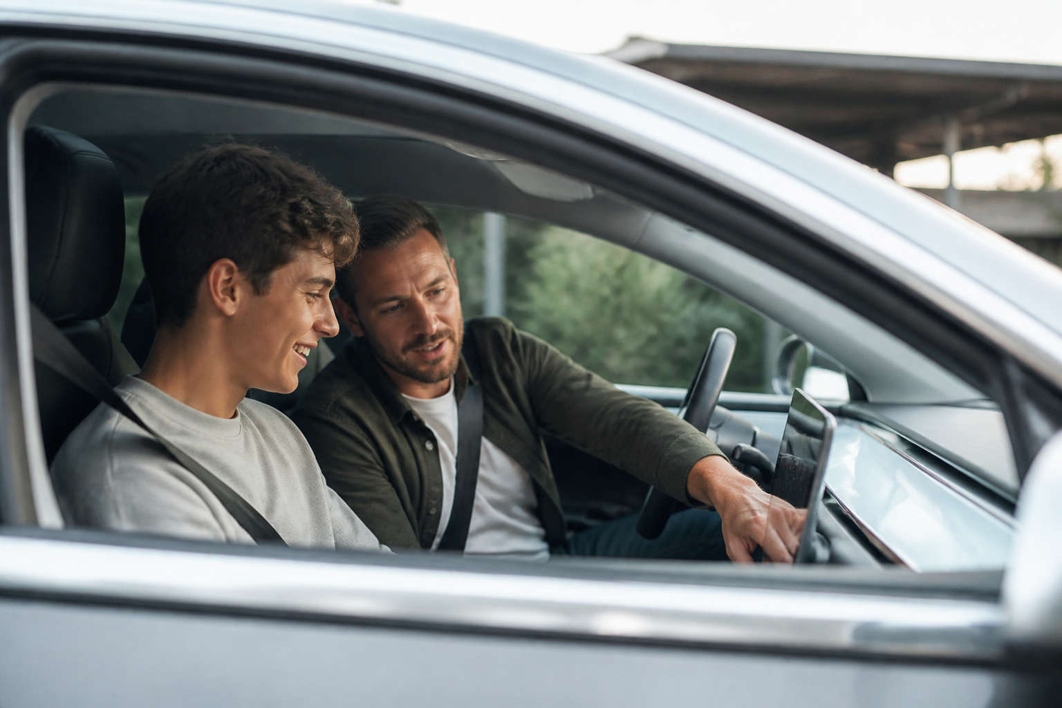 A young driver smiling while sitting in the driver's seat of a modern electric car, with a parent or instructor beside them, looking at the dashboard.